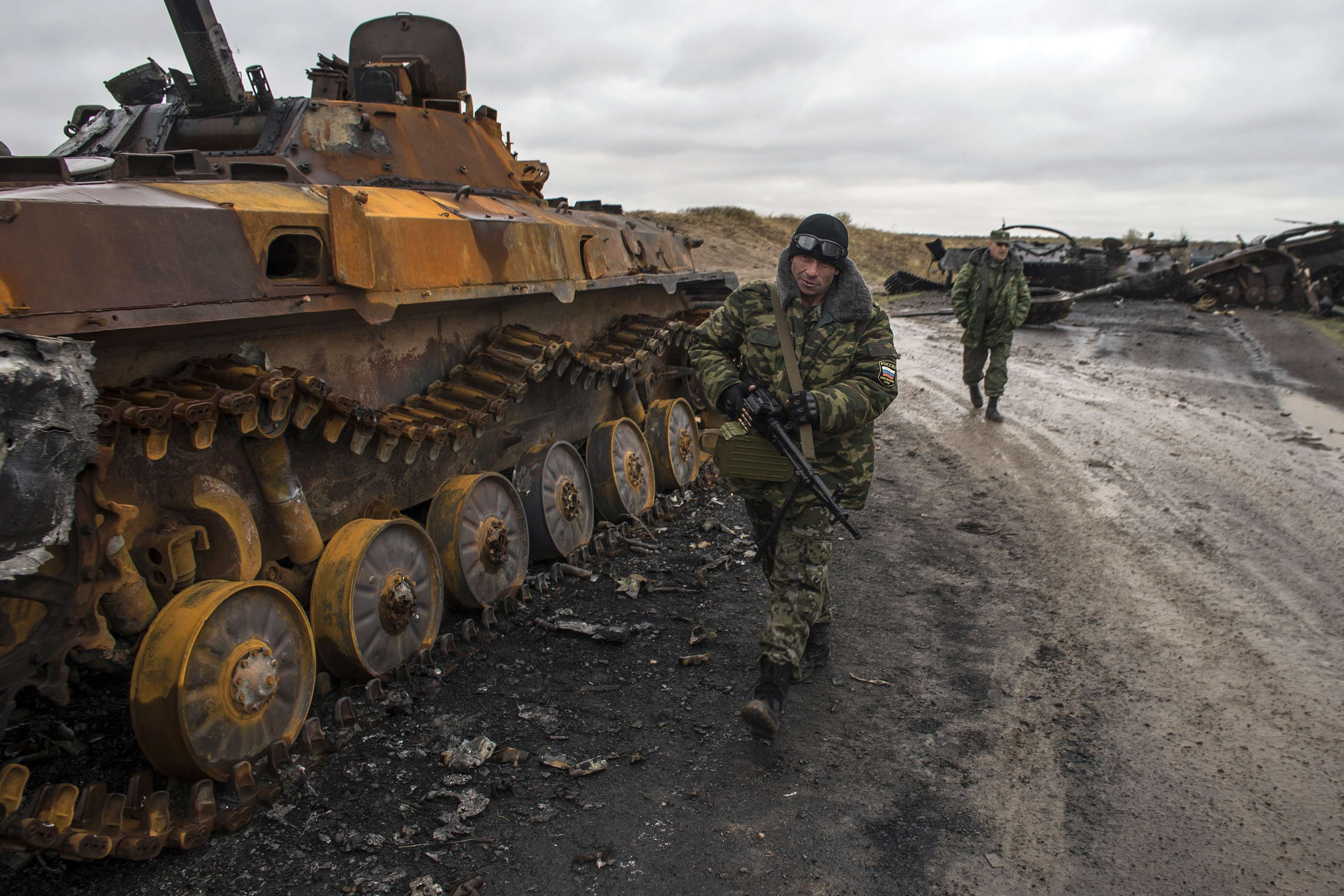 Pro-Russian rebels walk past a burnt-out Ukrainian armoured personnel carrier near the village of Novokaterinovka